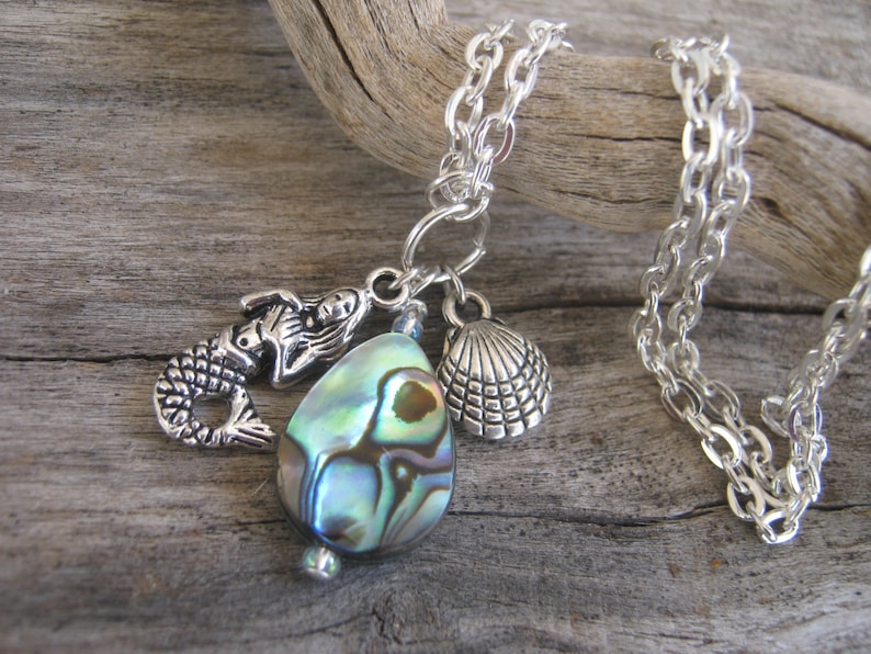 May include: A silver chain necklace with a mermaid charm, a shell charm, and a large iridescent abalone shell pendant.