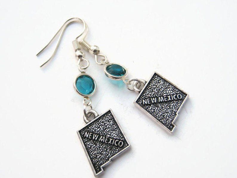 May include: Silver earrings with blue gemstone accents and a silver charm shaped like the state of New Mexico with the text "New Mexico" on it.