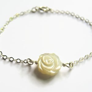 May include: A delicate silver chain bracelet with a white mother-of-pearl rose charm.