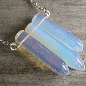 May include: A silver chain necklace with three iridescent opal teardrop pendants. The pendants are translucent and have a light blue and white colour.
