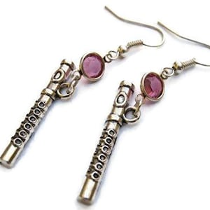 May include: Silver flute dangle earrings with pink crystal accents. The flute charm is detailed with a textured surface.