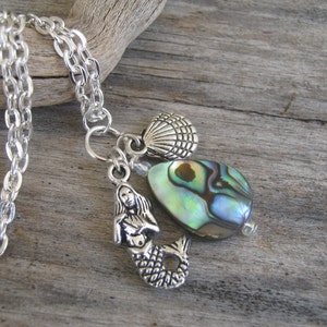 May include: Silver chain necklace with a mermaid charm, abalone shell bead, and a silver seashell charm.