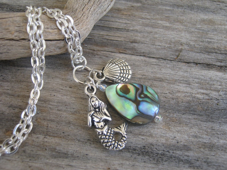 May include: Silver chain necklace with a mermaid charm, abalone shell bead, and a silver seashell charm.