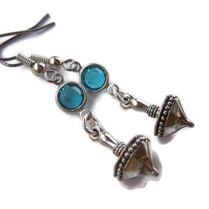 Puede incluir: Un par de pendientes de plata con piedras de cristal azul turquesa y un diseño de peonza.