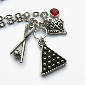 Puede incluir: Collar de cadena de plata con múltiples encantos, incluyendo un corazón rojo, un corazón de plata, un estante de bolas de billar de plata y un par de tacos de billar cruzados de plata con una bola de plata.