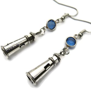 May include: Silver lighthouse earrings with blue crystal accents. The earrings are silver and have a lighthouse charm with a blue crystal on each earring.