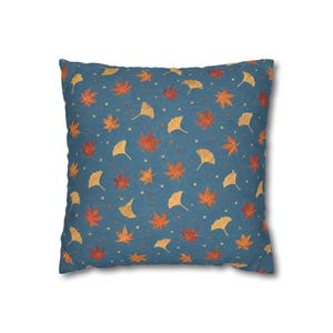Op de afbeelding: Een vierkant sierkussen met een donkerblauwe achtergrond en een herhalend patroon van oranje en rode esdoornbladeren, gele ginkgobladeren en kleine lichte stippen die gelijkmatig over het oppervlak van de stof zijn verspreid.