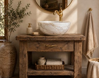 Puede incluir: Un mueble de baño de madera rústica con un lavabo de mármol blanco y grifo dorado, un cajón con tirador dorado y un estante inferior abierto con una cesta tejida, un tarro de cerámica y un paño doblado, además de una toalla beige colgada.