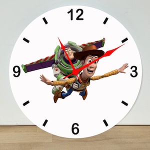 May include: A round white wall clock featuring a graphic of Buzz Lightyear and Woody from Toy Story in flight. The clock face has black numerals at the 3, 6, 9, and 12 positions, with black tick marks for other hours and red clock hands.
