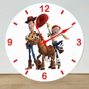 May include: A round wall clock with a white face featuring red numbers at 3, 6, 9, and 12. The center displays a graphic of a cowboy, a cowgirl, and a brown horse. The clock has red hour, minute, and second hands pointing toward the center.