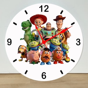May include: A round white wall clock featuring a colorful graphic of Toy Story characters including Woody, Buzz Lightyear, Jessie, Rex, Hamm, Mr. and Mrs. Potato Head, Slinky Dog, Bullseye, and the Aliens. The clock has black numbers and red hands.