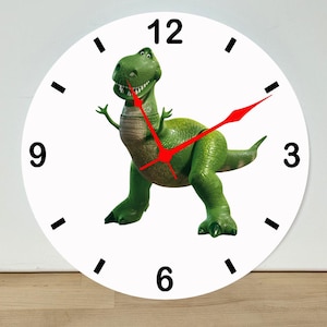 May include: A round white wall clock featuring a green Tyrannosaurus Rex dinosaur in the center. The clock face has black numerical markers for 3, 6, 9, and 12, along with simple black tick marks for the other hours. It includes bright red clock hands.