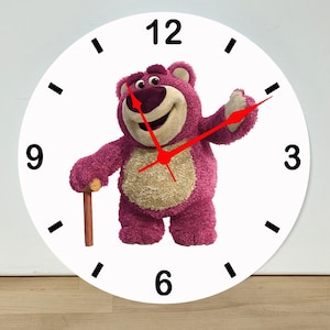 May include: A round wall clock with a white face, black hour markers, and black numerals at 3, 6, 9, and 12. The center features a purple bear character with a beige belly holding a brown cane. The clock has three thin, bright red hands.