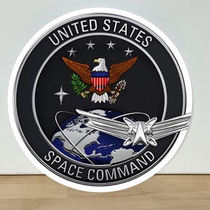 May include: A circular United States Space Command emblem featuring a black background with a central bald eagle holding an olive branch and arrows, a blue and white globe, silver wings, and the text UNITED STATES SPACE COMMAND in white letters.
