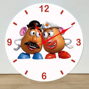May include: A round wall clock with a white face featuring Mr. and Mrs. Potato Head characters in the center. The clock has red numbers at the 3, 6, 9, and 12 positions, red tick marks for other hours, and thin red hour, minute, and second hands.