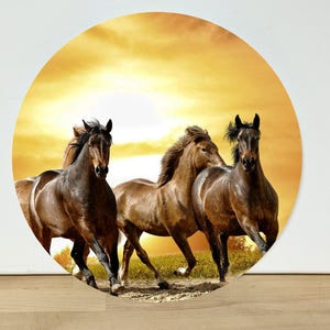 May include: A circular wall art piece featuring three brown horses galloping across a field. The background displays a bright yellow and orange sunset sky. The horses are depicted in motion, with their manes flowing as they run forward together.