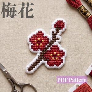 以下が含まれることがあります： 梅の花の枝をクロスステッチで刺繍した作品。濃い赤色の花びら、黄色の中心部、茶色の枝で構成され、白い糸で縁取られている。左上に「梅花」、右下に「PDF Pattern」という文字が配置されている。