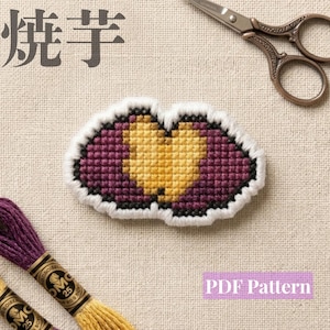 May include: A cross-stitch embroidery piece featuring a central golden yellow heart shape surrounded by a deep purple background, all outlined in white thread. The image includes metal scissors, purple and gold embroidery floss, and the text 焼芋.