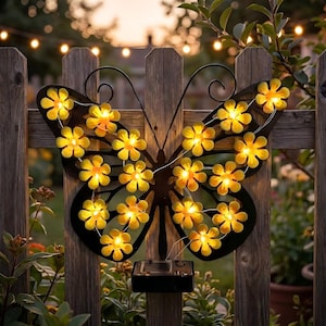 Pode incluir: Uma decoração de parede com silhueta de borboleta em metal preto, apresentando um fio de luzes LED amarelas em forma de flor fixadas à estrutura. Uma pequena caixa de painel solar retangular está montada no centro inferior da borboleta.