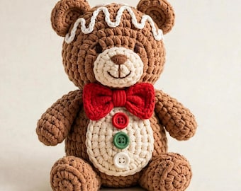 May include: A brown crochet teddy bear designed to resemble a gingerbread person. It features white wavy icing-like trim on its head, a bright red bow tie, and three round buttons in red, green, and white on its cream-colored belly.