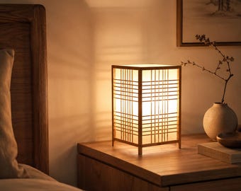 May include: A rectangular table lamp with a light-colored wooden frame and a grid-patterned lattice overlay. The lamp emits a warm, soft glow through its translucent panels, casting distinct shadows on the surrounding wall surface.