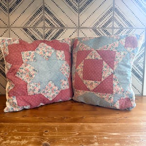 May include: Two square throw pillows featuring patchwork quilt designs. The left pillow displays a central blue star surrounded by floral and dusty rose patterned fabric. The right pillow features a geometric star pattern in blue, rose, and floral prints.
