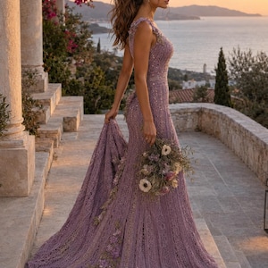 May include: A floor-length lavender lace gown featuring intricate floral embroidery, a fitted bodice, and a sweeping train. The dress is adorned with delicate beadwork and textured patterns throughout, paired with a bouquet of dried flowers.