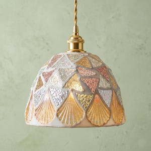 Puede incluir: Una lámpara colgante en forma de cúpula con un patrón de mosaico de fragmentos de vidrio iridiscente, ámbar y transparente. La pantalla tiene un herraje de metal dorado y cuelga de un cable trenzado de color dorado a juego.