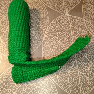 May include: A bright green crocheted object consisting of a cylindrical vertical section attached to a horizontal, slightly curved base. The item is crafted from yarn with a visible textured stitch pattern throughout its entire structure.