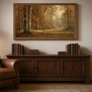 Puede incluir: Un cuadro de paisaje rectangular en un marco de madera que representa una escena forestal con follaje otoñal en tonos marrón, dorado y naranja. La obra de arte se exhibe en una pared sobre un aparador de madera marrón oscuro con libros.