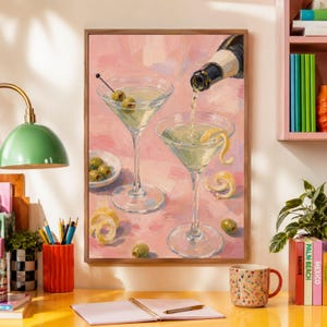 Pode incluir: Uma pintura a óleo numa moldura de madeira representando dois copos de martini cheios de um líquido transparente sobre um fundo rosa texturado. Um copo contém azeitonas verdes num palito, enquanto o outro é enchido a partir de uma garrafa, com uma espiral de limão.