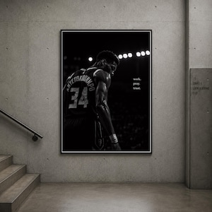 Peut inclure: Une impression d'art murale encadrée en noir et blanc représentant un joueur de basket-ball de dos, portant un maillot avec le nom ANTETOKOUNMPO et le numéro 34. Le texte work. pray. trust. est imprimé à droite sur un fond sombre.
