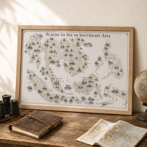 Op de afbeelding: Een ingelijste kaart met de titel Places to See in Southeast Asia, met gedetailleerde illustraties van bezienswaardigheden in de regio. De kaart zit in een lichthouten lijst en heeft een beige achtergrond met zwarte inkttekeningen.
