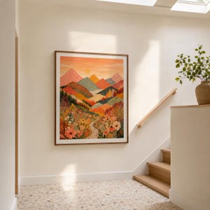 Puede incluir: Una impresión artística enmarcada que presenta una ilustración de paisaje con montañas superpuestas en tonos naranja, rosa, verde y amarillo, sobre un primer plano lleno de flores silvestres detalladas y un sendero bajo un cielo de atardecer.