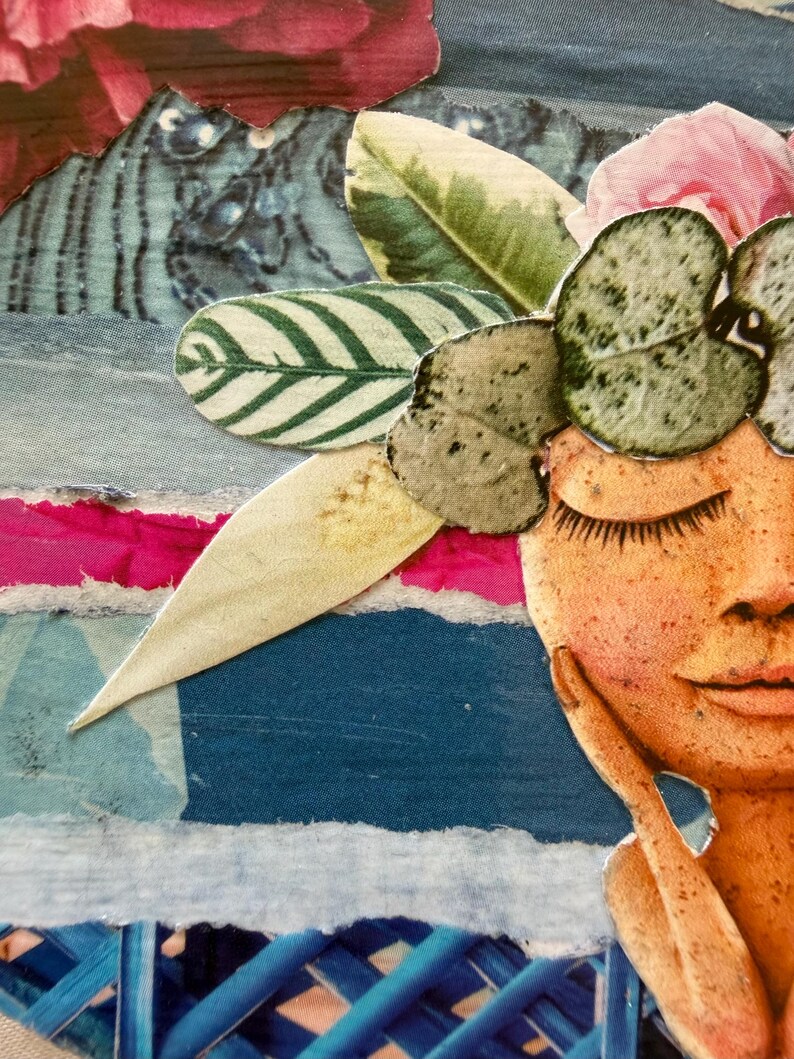 May include: A mixed media collage artwork featuring a stylized face with closed eyes and freckles, adorned with a crown of paper cut-out green leaves and pink flowers, set against a layered background of blue, white, and magenta paper strips.
