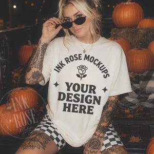 Pode incluir: Uma t-shirt de manga curta em tom off-white com texto preto que diz INK ROSE MOCKUPS, um ícone de rosa e YOUR DESIGN HERE, acompanhado por duas estrelas de quatro pontas. A t-shirt é combinada com calções aos quadrados pretos e brancos.