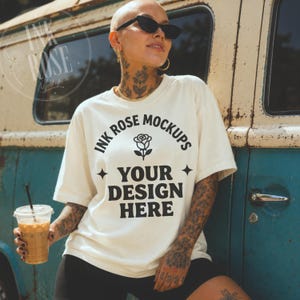 May include: An off-white short-sleeve t-shirt featuring black text that reads INK ROSE MOCKUPS, a rose icon, and YOUR DESIGN HERE, accented by two four-pointed stars. The shirt is worn with black shorts and a clear plastic cup of iced coffee.