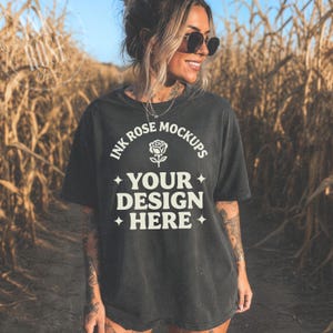 May include: A charcoal gray short-sleeve t-shirt featuring white text that reads INK ROSE MOCKUPS with a rose icon above the words YOUR DESIGN HERE and four-pointed star accents. The shirt has a crew neckline and a relaxed, loose-fitting cut.
