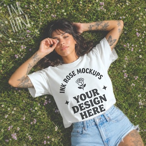 May include: A white short-sleeved t-shirt featuring the black text INK ROSE MOCKUPS YOUR DESIGN HERE with a rose icon and star accents. The shirt is paired with light blue denim shorts, showcasing a casual style for display purposes.