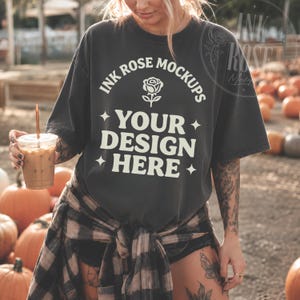 May include: A charcoal gray short-sleeve t-shirt featuring the white text INK ROSE MOCKUPS, a rose icon, and the text YOUR DESIGN HERE, accented with four-pointed stars. The shirt has a crew neckline and a relaxed, loose-fitting silhouette.