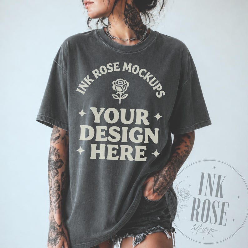 K&ouml;nnte beinhalten: Ein anthrazitfarbenes Kurzarm-T-Shirt mit Vintage-Waschung. Auf der Vorderseite befindet sich cremefarbener Text mit der Aufschrift INK ROSE MOCKUPS, ein Rosen-Symbol und die Worte YOUR DESIGN HERE, akzentuiert durch vierzackige Sterne an den Seiten.