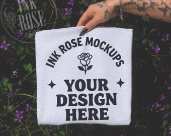 White Comfort Colors 1717 handheld mockup, foto gevouwen shirt, getatoeëerde hand, donkere bloementuin, edgy boutique T-shirt