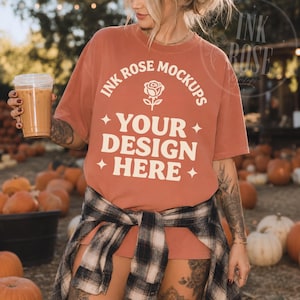 May include: A terracotta-colored short-sleeve t-shirt featuring cream-colored text that reads INK ROSE MOCKUPS YOUR DESIGN HERE with a small rose icon and four-pointed star accents. A black and white plaid flannel shirt is tied around the waist.