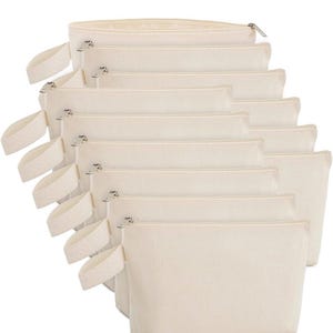 May include: A stack of eight rectangular off-white canvas pouches arranged in a cascading row. Each pouch features a top zipper closure with a silver-toned metal pull and a matching fabric wrist strap attached to the left side of the bag.