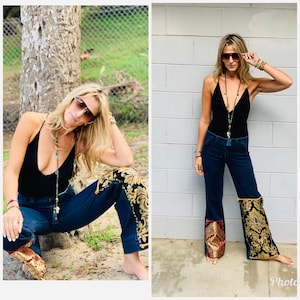 May include: A woman wearing a black tank top, dark blue jeans with gold and burgundy embroidered accents, and sunglasses. She is wearing a long beaded necklace with a turquoise tassel.