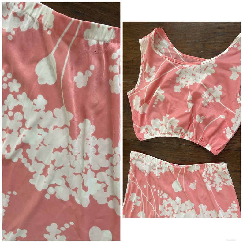 May include: A pink two-piece outfit with a white floral print. The top is a sleeveless crop top and the bottom is a skirt.