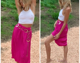 May include: A woman wearing a white tank top and a bright pink skirt with a silver chain belt. The skirt is knee-length and has a slight A-line shape.