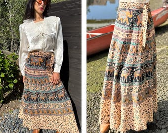 May include: A long, flowing wrap skirt with an intricate pattern of elephants and paisley designs in shades of brown, blue, and beige. The skirt is tied at the waist with a matching fabric belt.