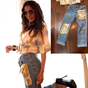 May include: A woman wearing a white and gold patterned crop top with a pair of blue denim jeans. The jeans have patches of fabric sewn on the front pockets and the legs are cuffed. The woman is wearing black high heels and sunglasses.