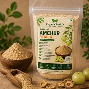 Peut inclure: Un sachet transparent contenant de la poudre d'Amchur naturelle OrganicSeedsIN, avec une étiquette beige portant du texte vert et des illustrations de fruits amla. Le sachet est entouré d'un bol en bois, d'une pelle et de fruits amla frais.